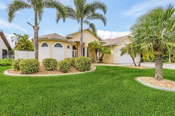 A residential house with a well-maintained lawn, palm trees, and a gated driveway. - Dream villa with tropical garden on the canal (Cape Coral)