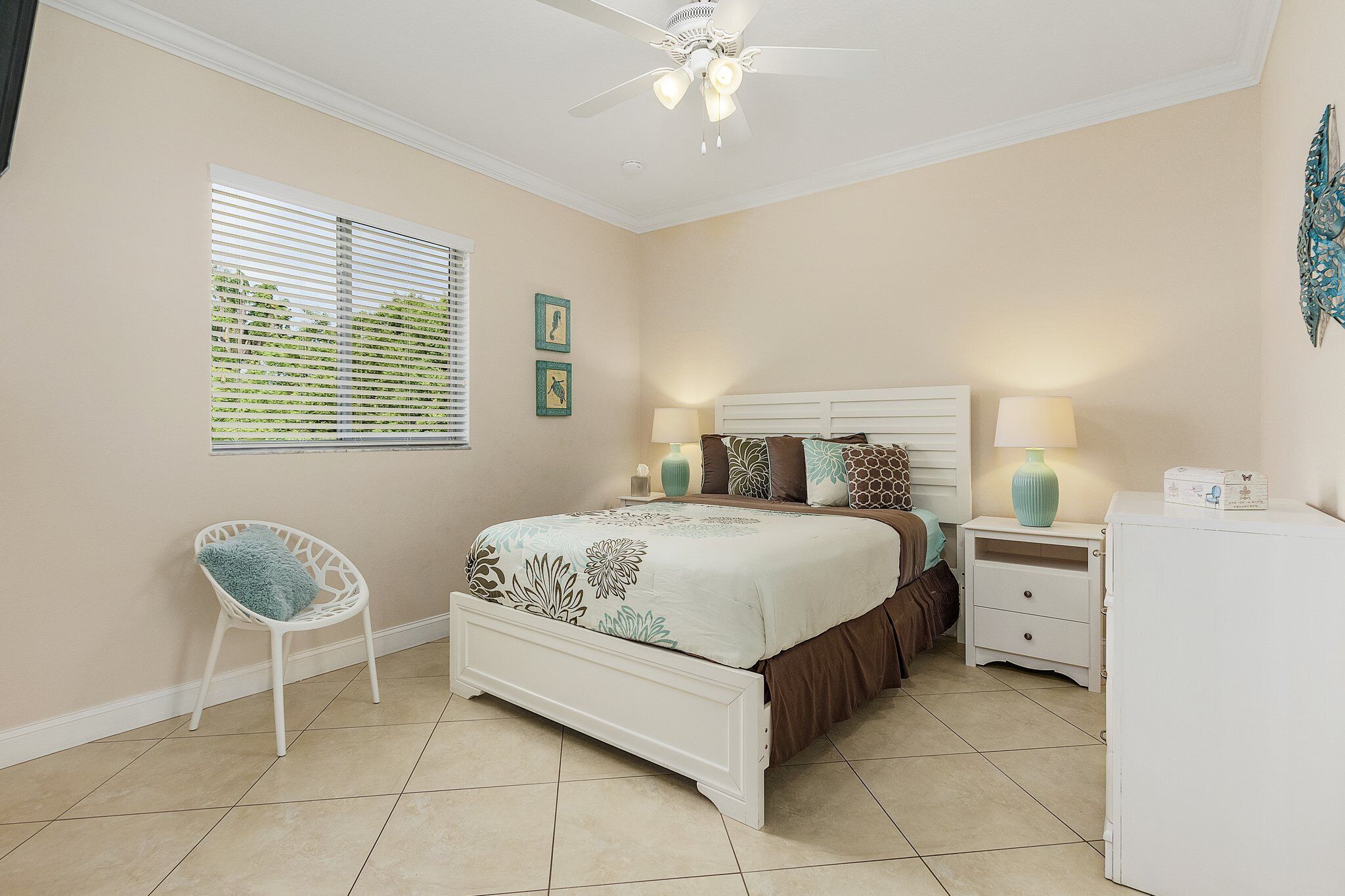 A bedroom with a bed, nightstands, a chair, a ceiling fan, and a window with blinds.
