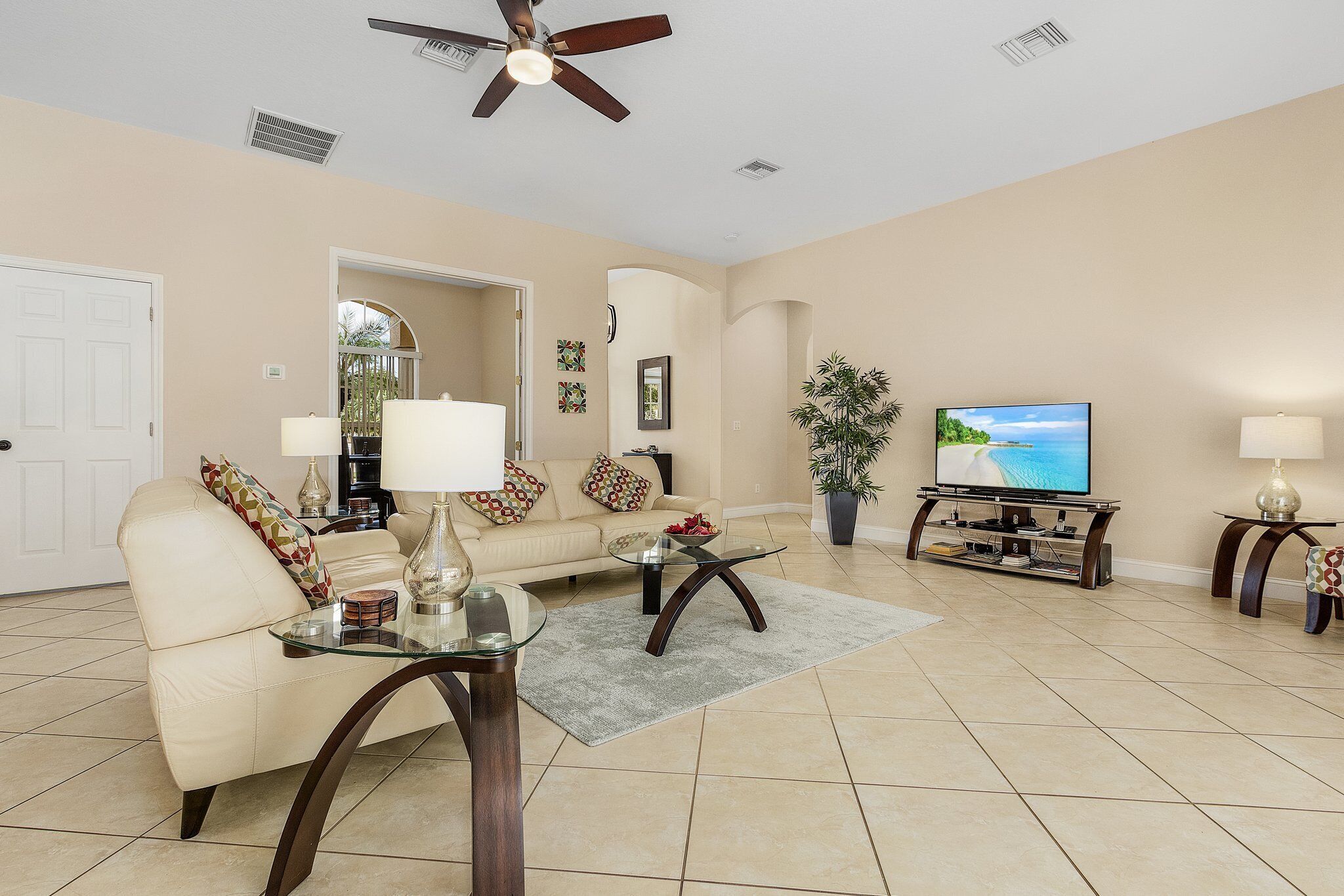 A living room with a beige sofa, two glass coffee tables, a TV, and a ceiling fan.