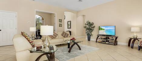 A living room with a beige sofa, two glass coffee tables, a TV, and a ceiling fan.