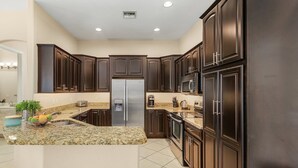A modern kitchen with dark wood cabinets, granite countertops, stainless steel appliances, and a central island with a fruit bowl. - Dream villa with tropical garden on the canal (Cape Coral)