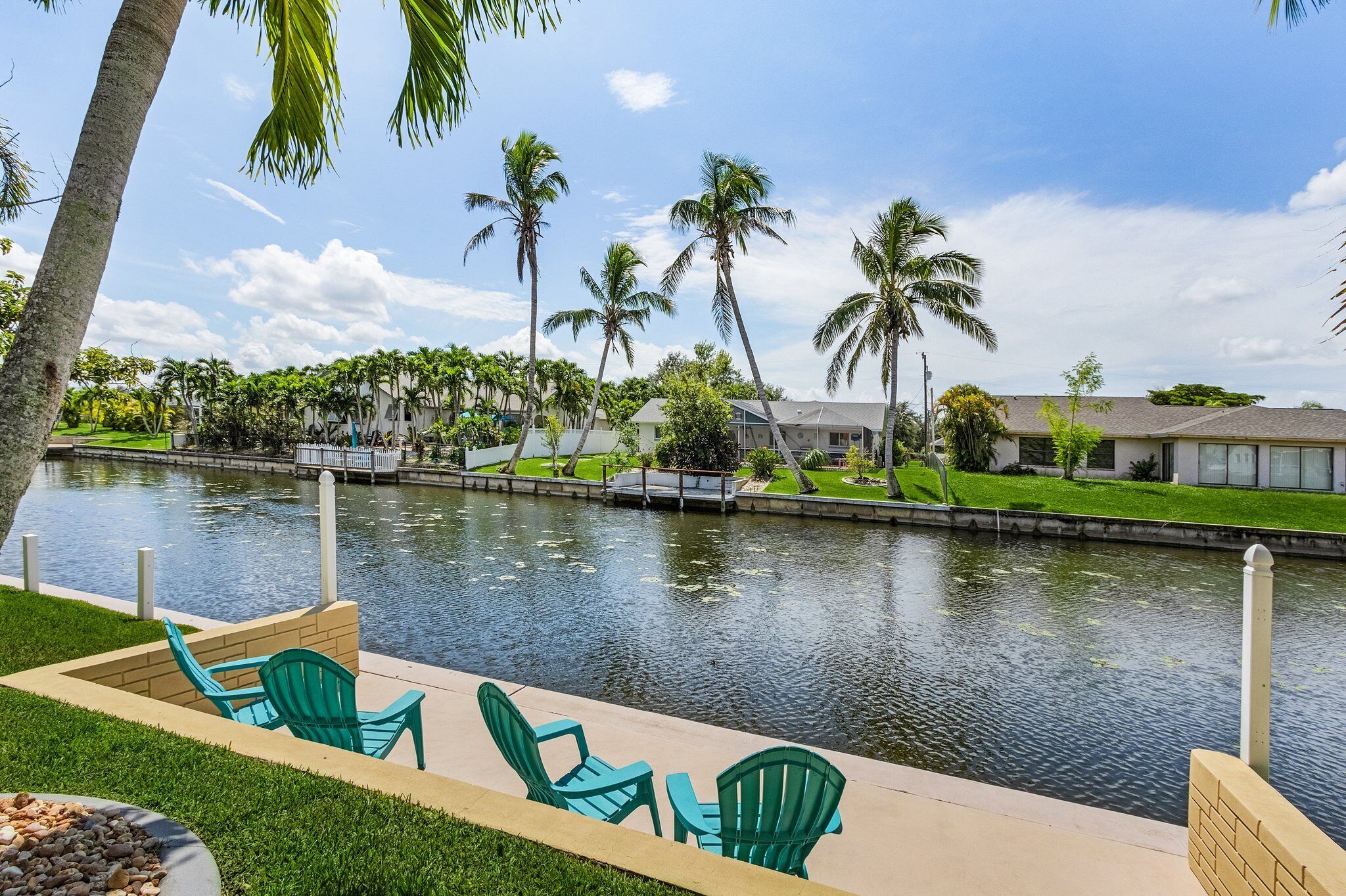 A serene outdoor area with a water feature, green chairs, and palm trees.