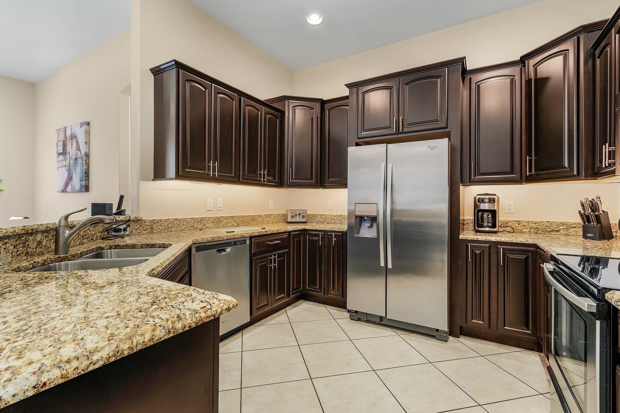 A kitchen with dark wood cabinets, a stainless steel refrigerator, granite countertops, and a dishwasher.