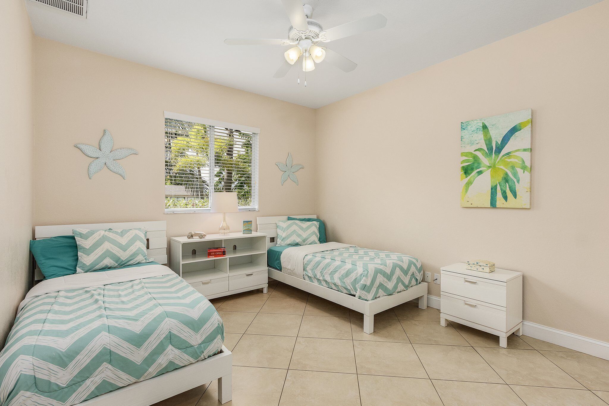 A bedroom with two beds, a ceiling fan, a window with blinds, and a wall-mounted shelf.
