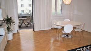 A modern dining area with a round table and white chairs, a potted plant, and a view of a building through a window.