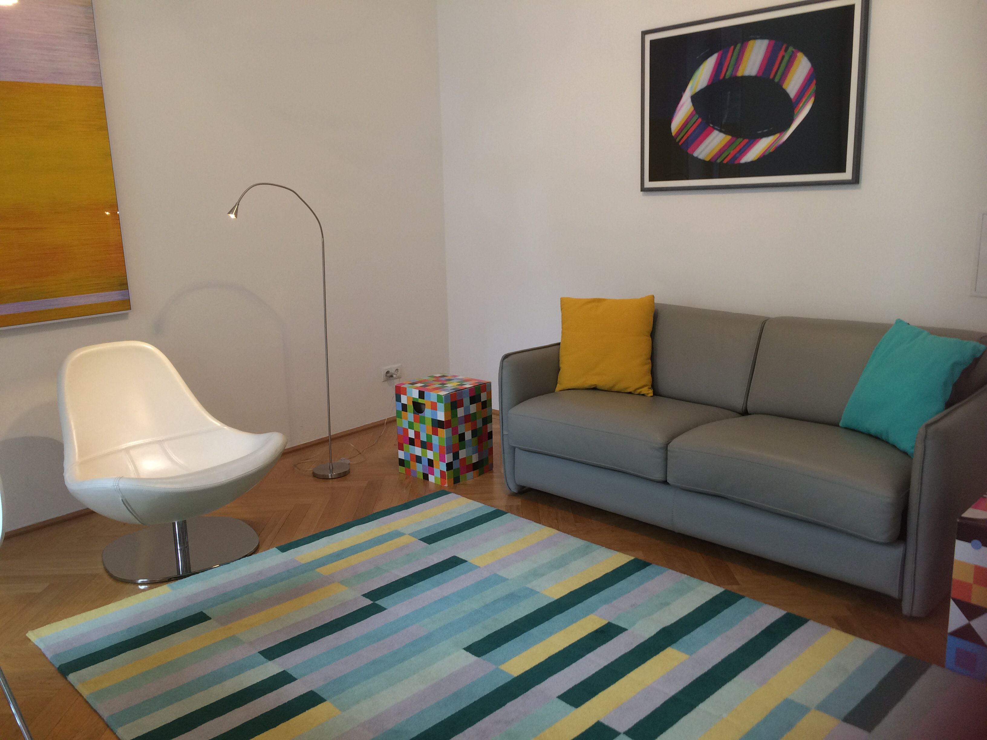 En moderne stue med en grå sofa, en hvid stol, et farverigt tæppe og en gulvlampe.