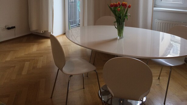 A modern dining area with a white table, two white chairs, a vase with red flowers, and a unique paper-like pendant light.
