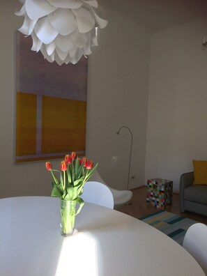 A modern living room with a white table, a glass vase with red tulips, a colorful geometric side table, and a large abstract painting on the wall. - Absolute quiet location with balcony and still in a few minutes in the center (wien)