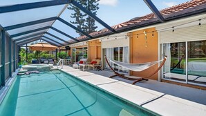Un área de piscina con un patio con paredes de vidrio, asientos al aire libre y una hamaca.