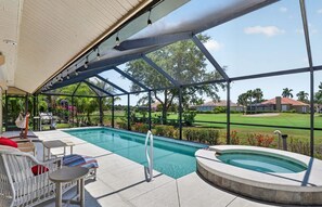 A covered outdoor swimming pool with lounge chairs and a hot tub, surrounded by a metal frame and glass panels.