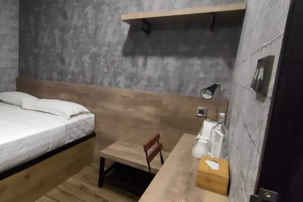 A small, compact room with a single bed, a wooden table, and a chair.