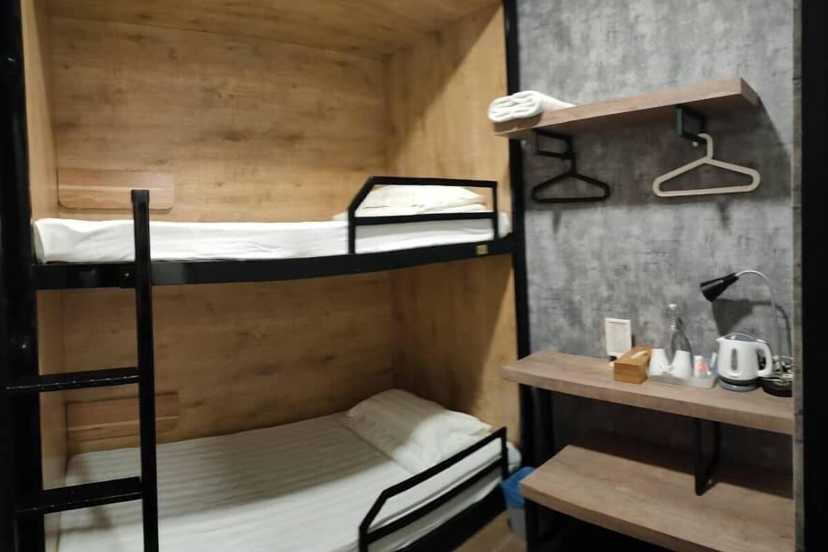 A bunk bed room with wooden walls, a small desk, and a hanging light.