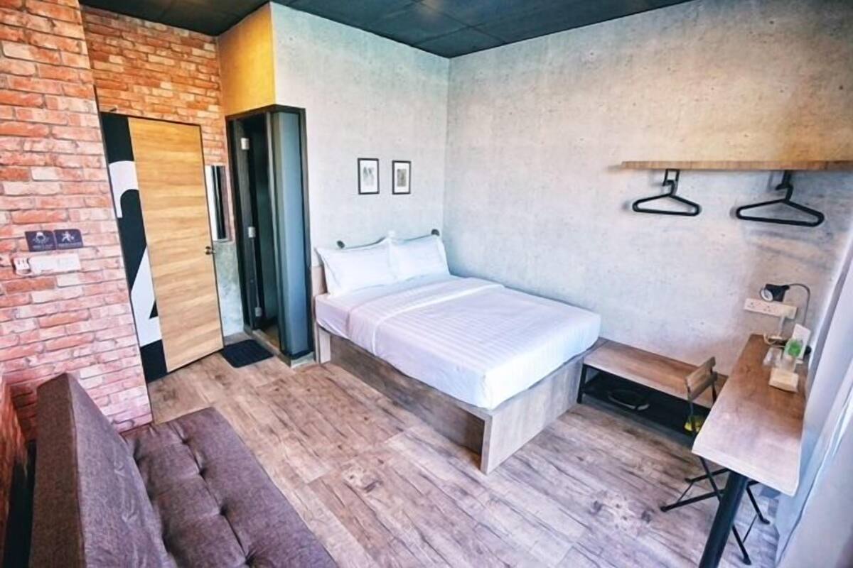 A bedroom with a bed, a bench, a desk, and a hanging clothes rack.