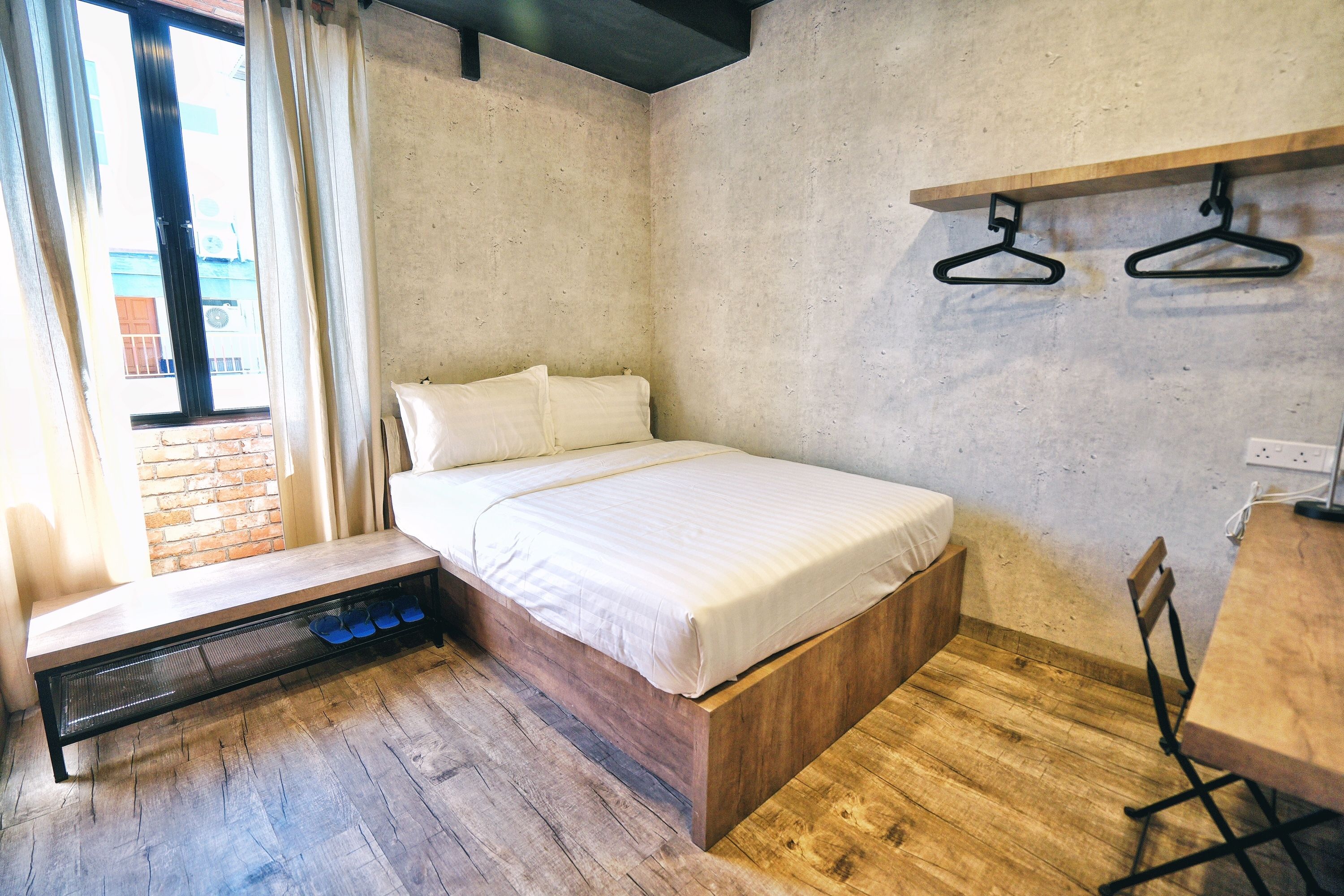 Een kleine, moderne kamer met een bed, een opbergbank, een houten tafel en uitzicht door een raam.