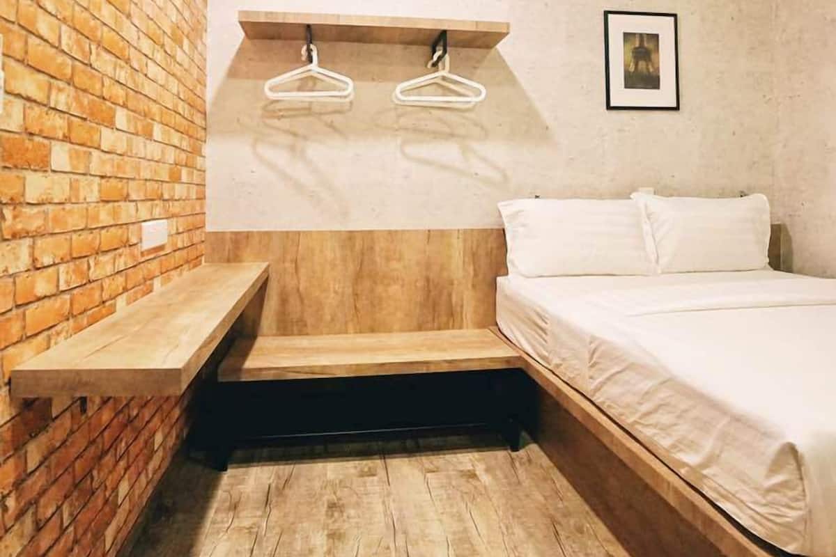 A small, cozy room with a brick wall, a wooden bench, a bed, and a hanging light fixture.