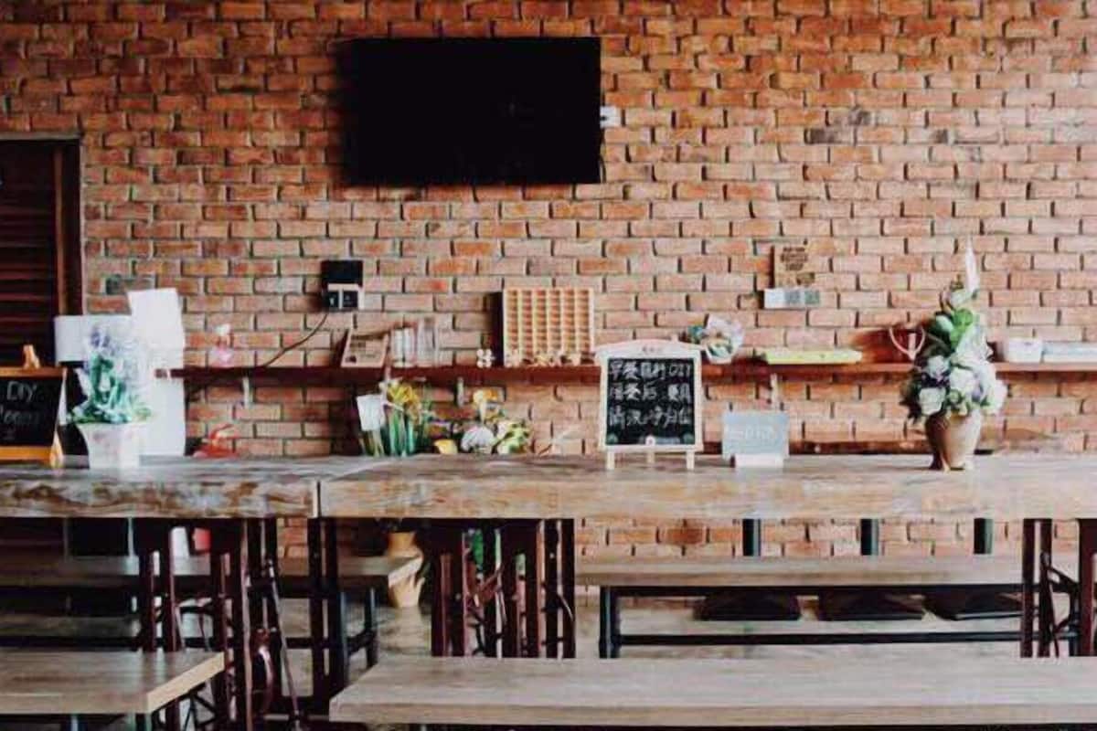 A rustic brick wall with a dartboard and chalkboards, wooden tables, and benches in a cafe setting.
