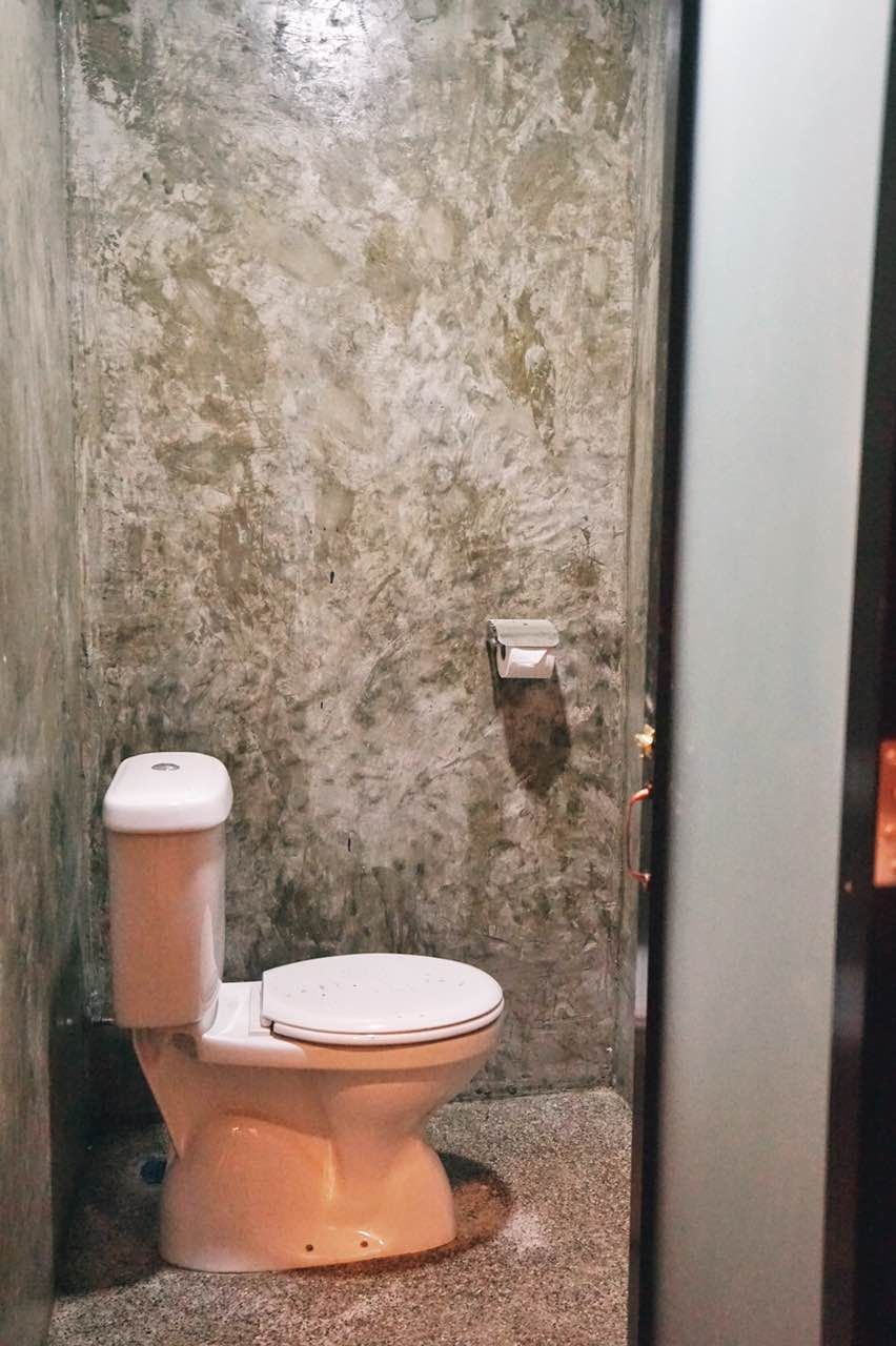 A toilet in a bathroom with a textured wall and a visible toilet paper holder.