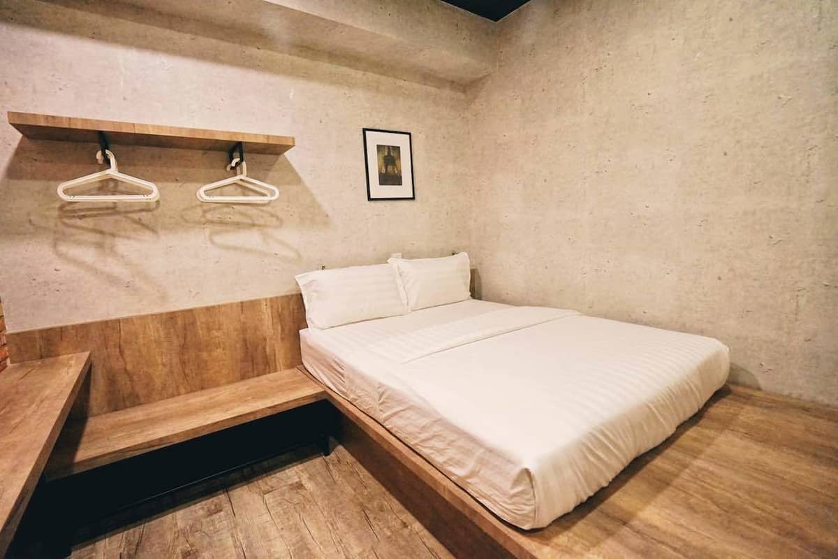 A bedroom with a wooden platform bed, a wooden bench, and two white hangers on a wall-mounted shelf.