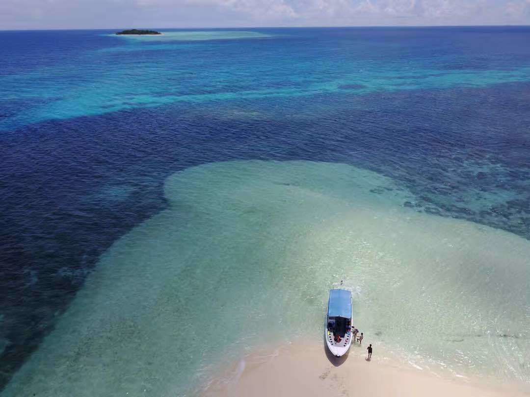 An aerial view of a beach with a boat anchored near the shore.