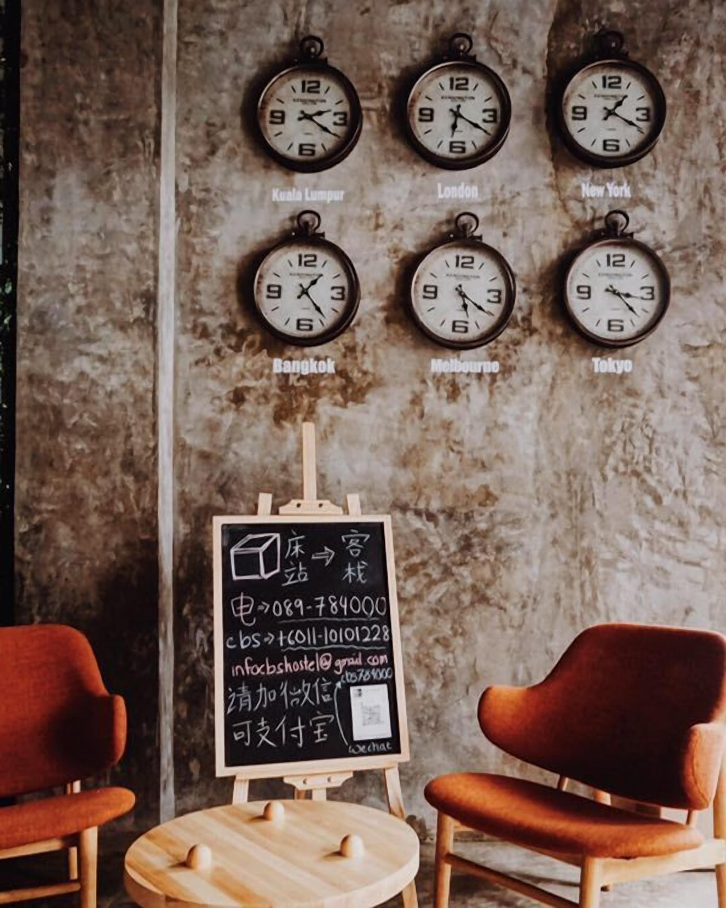 A wall with clocks showing different times for Kuala Lumpur, London, New York, Bangkok, Melbourne, and Tokyo. Below the clocks, there is a chalkboard with contact information.