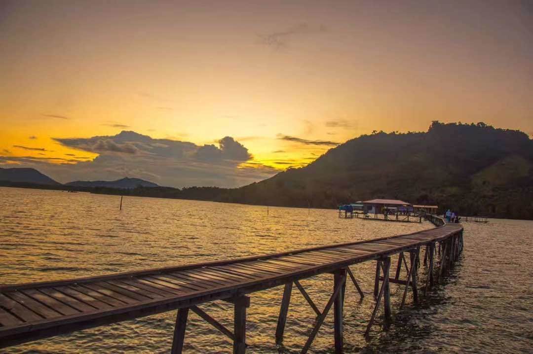 Een houten steiger die zich uitstrekt over kalm water, met een zonsondergang op de achtergrond.