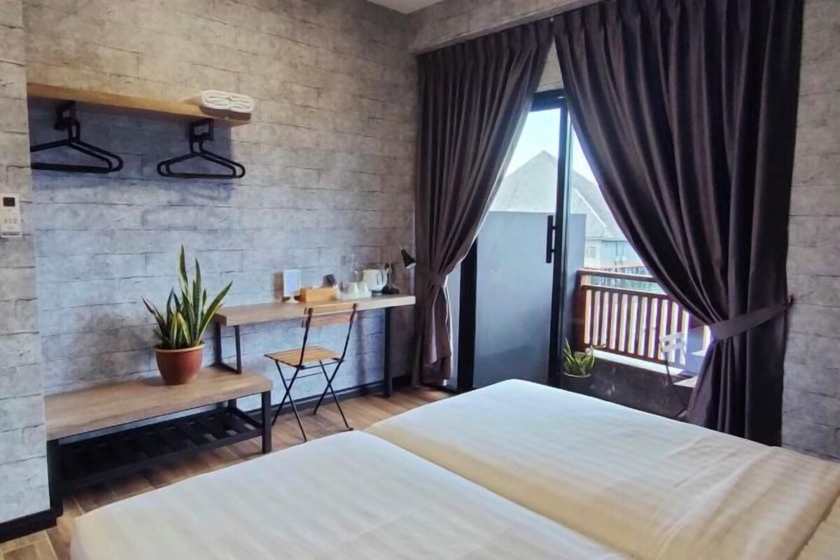 Quarto de hotel moderno com cama, escrivaninha, cadeira e varanda com guarda-corpo.