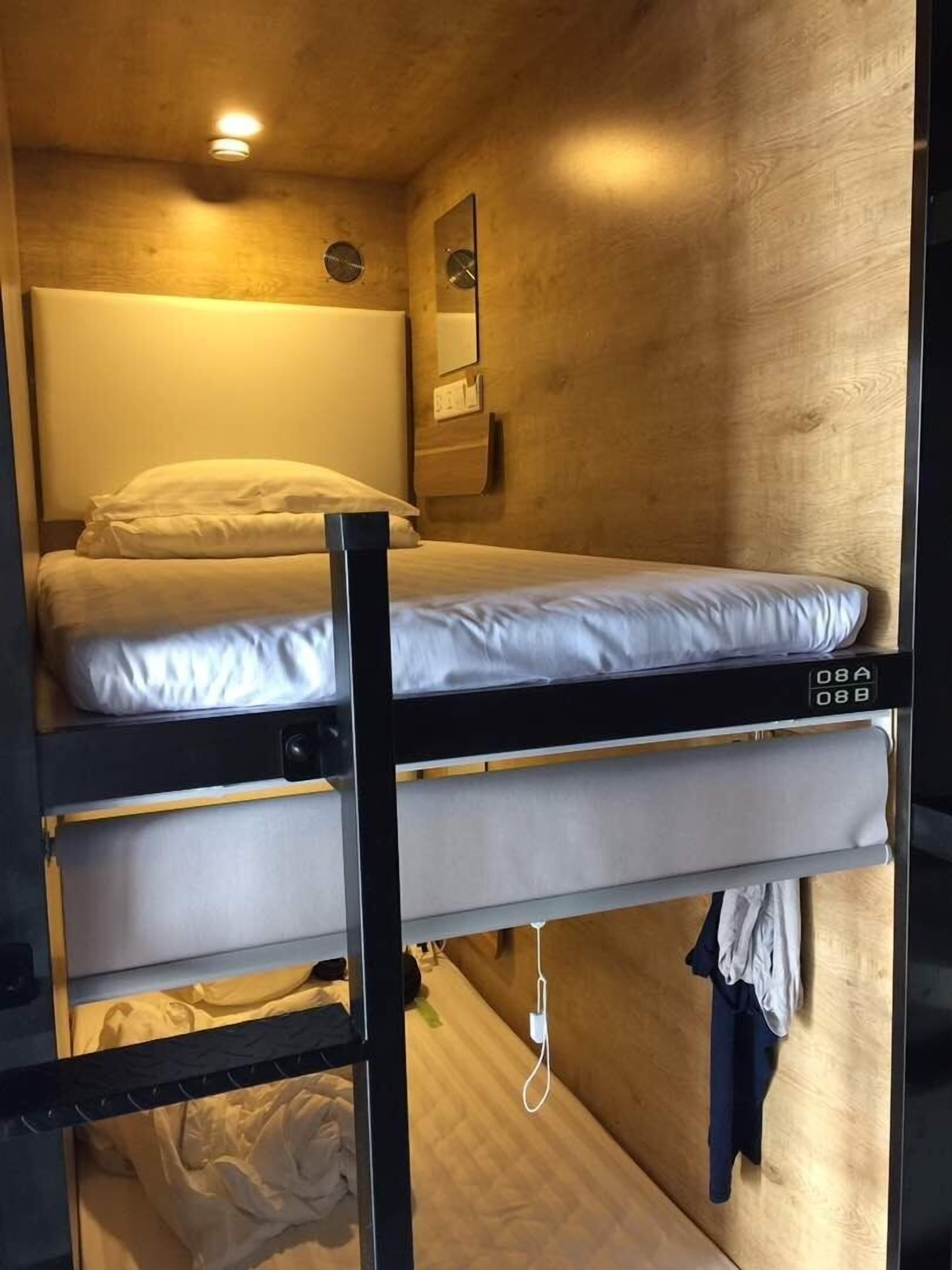 Un lit superposé avec une tête de lit, un miroir et un luminaire fixé au mur.