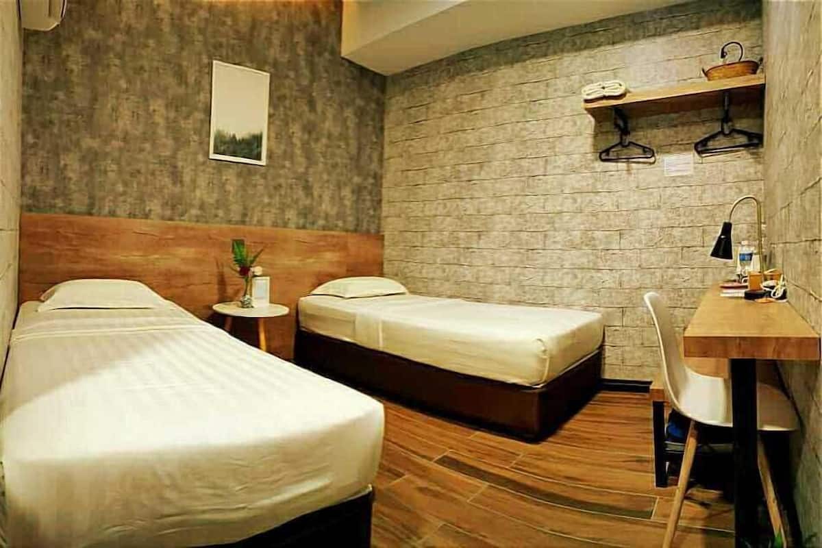 A hotel room with two beds, a wooden headboard, a small table with a lamp, and a desk with a chair.