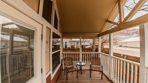 A covered porch with a wooden deck, two chairs, and a small table.