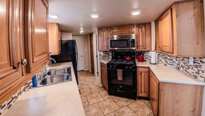 A compact kitchen with wooden cabinets, a stainless steel sink, a black refrigerator, a microwave, and a stove.