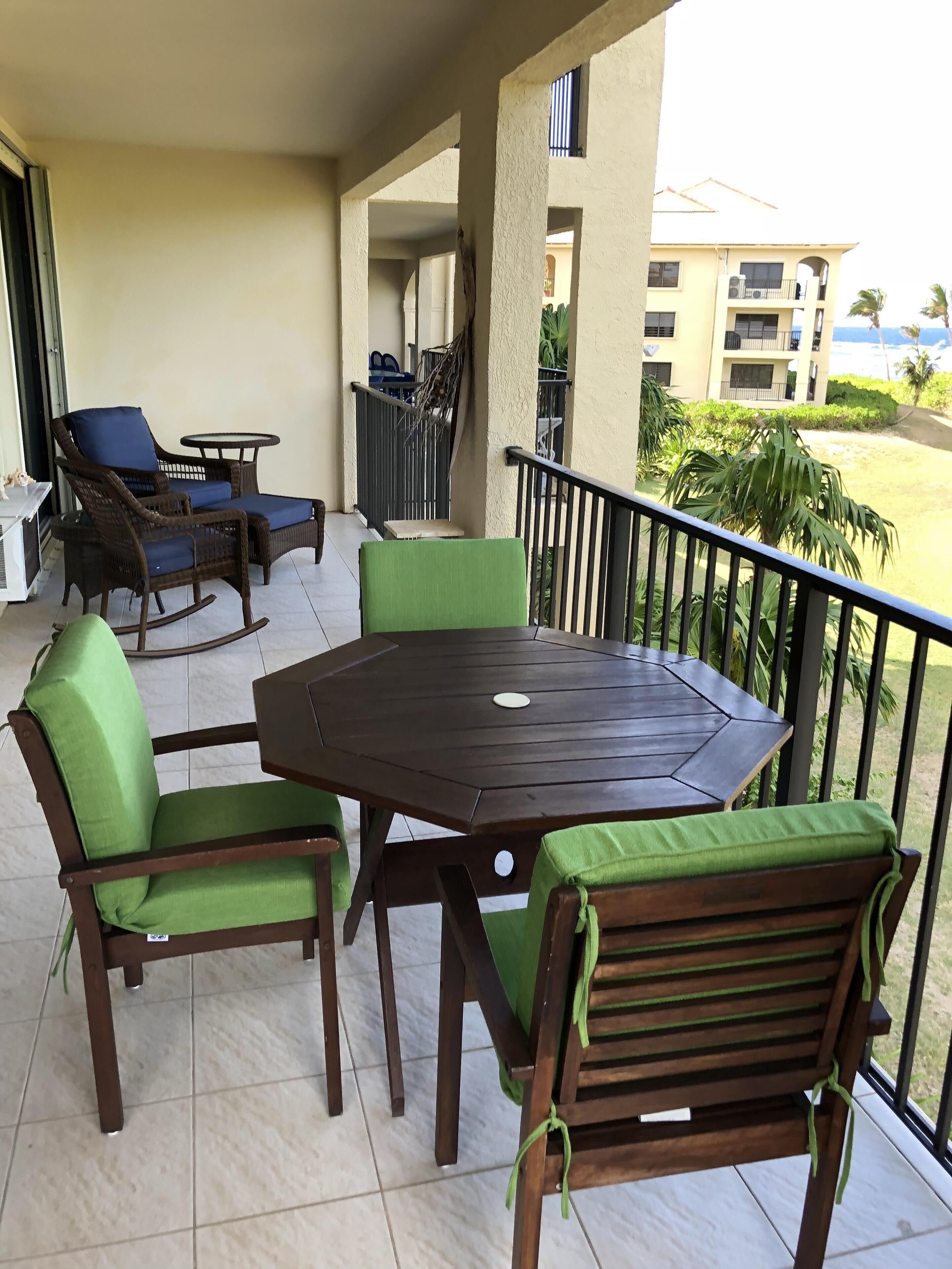 A balcony with a wooden table and chairs, a small table, and a chair with a green cushion.