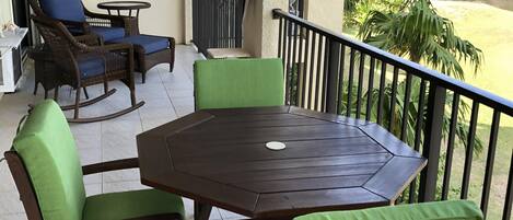 A balcony with a wooden table and chairs, a small table, and a chair with a green cushion.