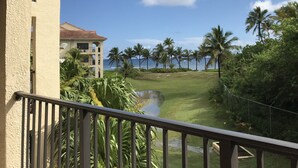 Une vue depuis un balcon donnant sur un terrain de golf, avec un plan d’eau, des palmiers et un bâtiment dont le toit est recouvert de tuiles rouges.
