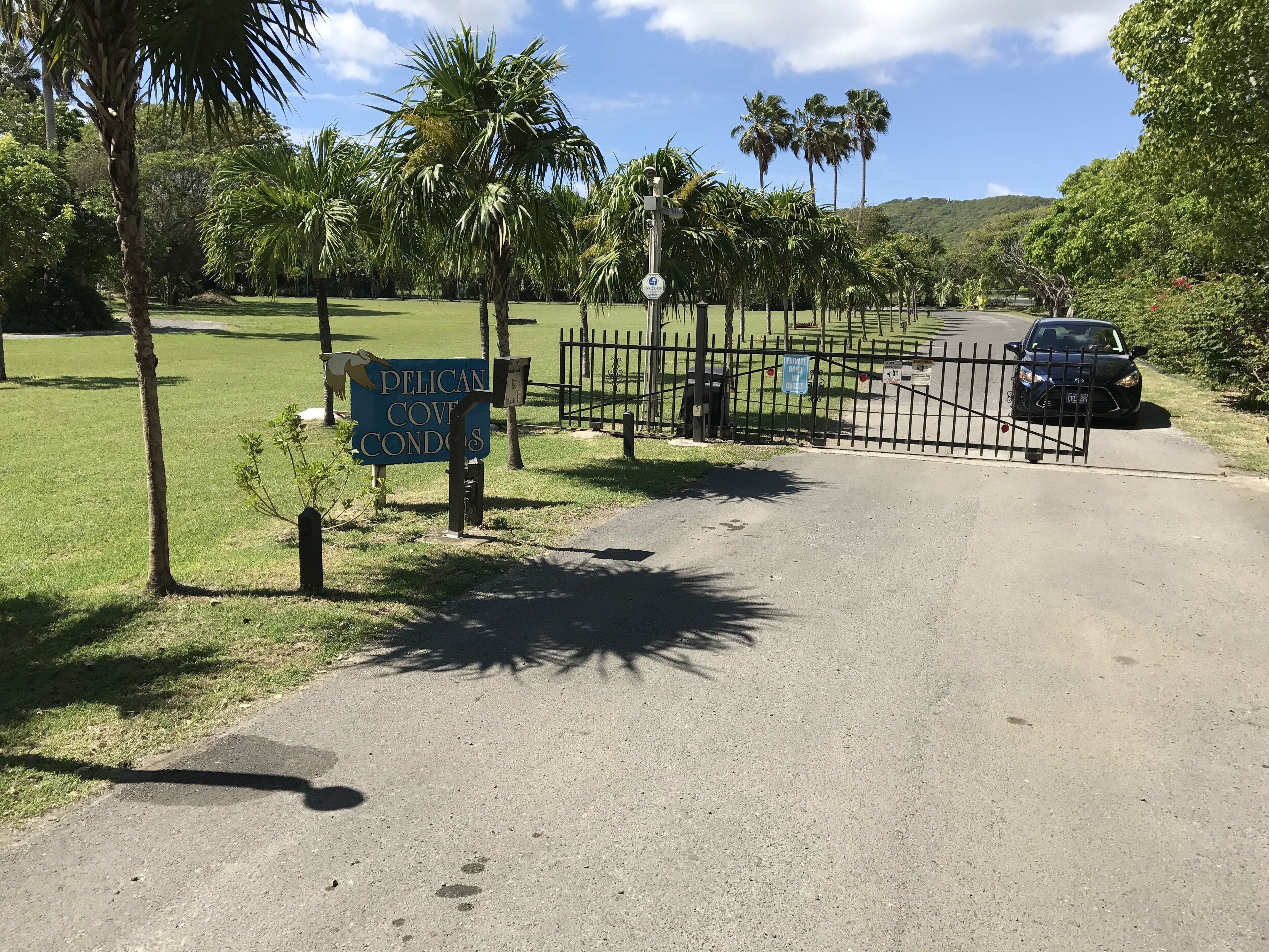 A gated entrance to a property named Pelican Cove Condos, with a signboard and a black car parked nearby.