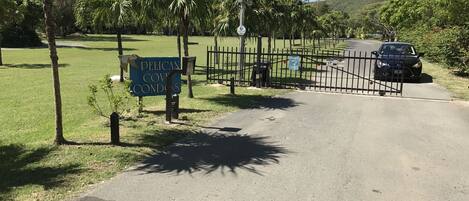 A gated entrance to a property named Pelican Cove Condos, with a signboard and a black car parked nearby.