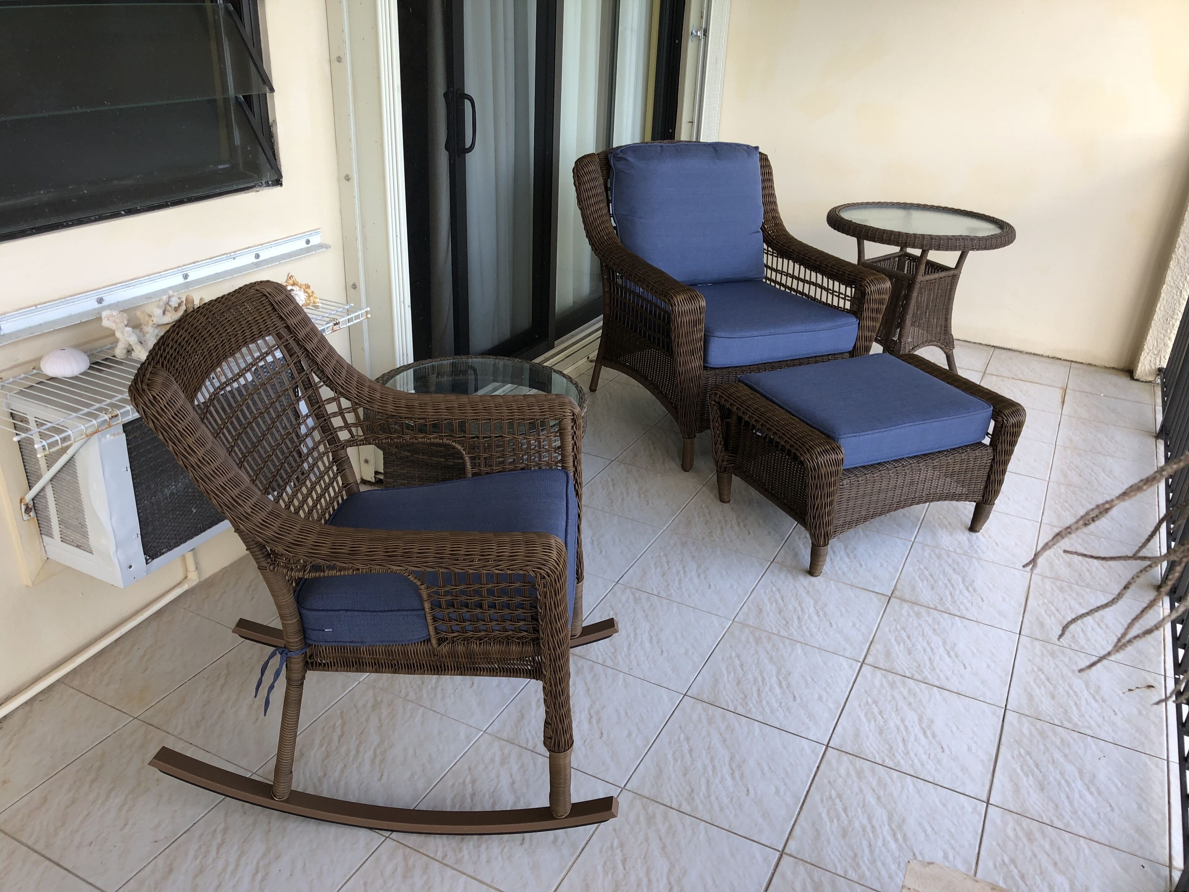 A balcony with wicker furniture, including a rocking chair and a table, and a glass enclosure.