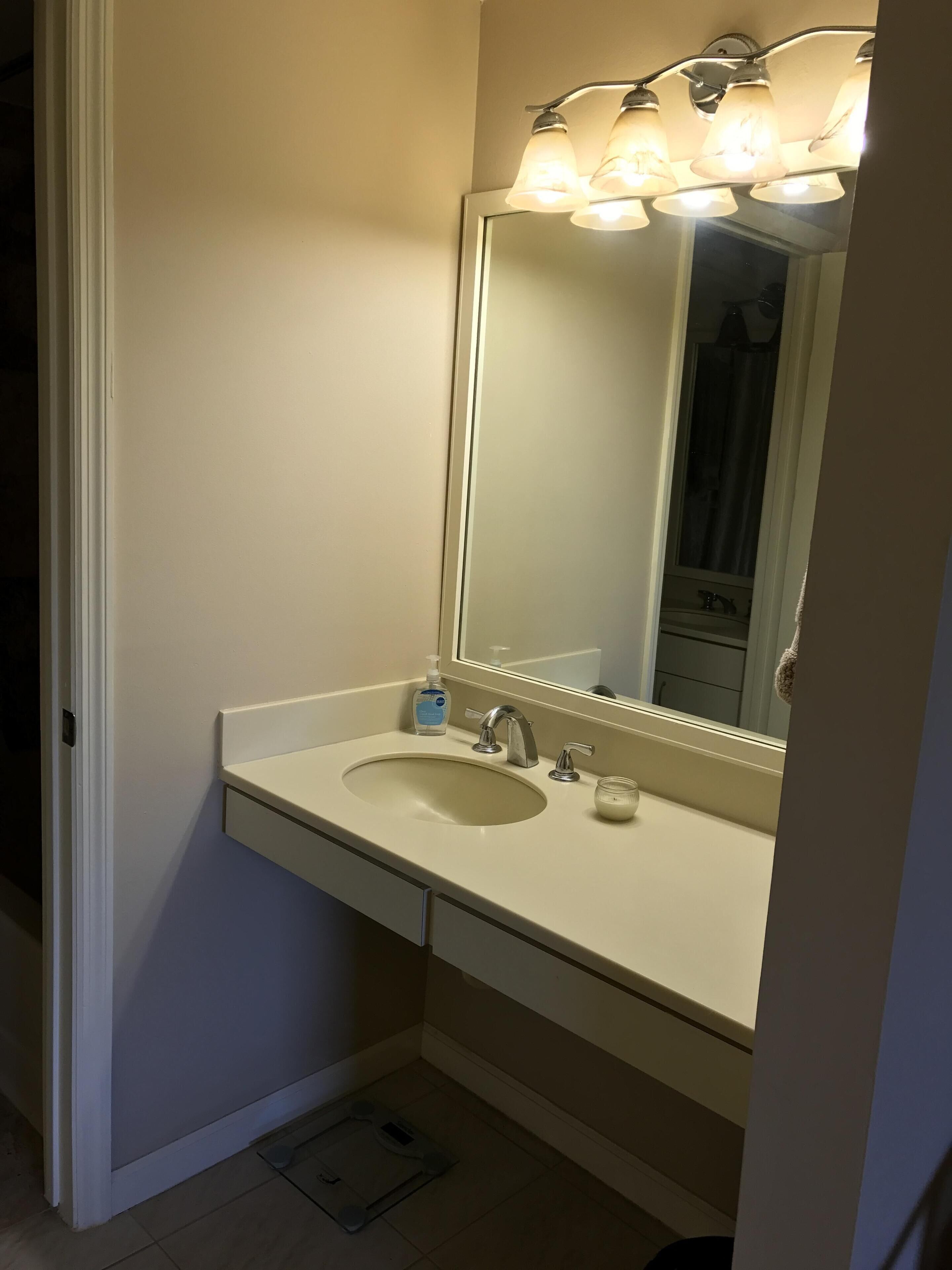 Une salle de bain avec un lavabo, deux robinets, un miroir et un luminaire placé au-dessus du miroir.