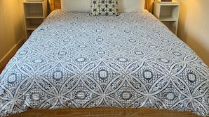 A bed with a patterned bedspread, two bedside lamps, a wooden headboard, and a window with curtains. - Great Location, Clean, Beachy 1BR Cottage (Haiku-Pauwela)