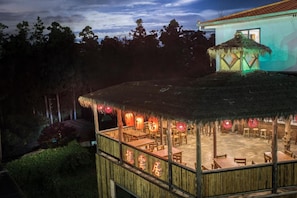 A restaurant with a thatched roof and bamboo railing, featuring tables and chairs arranged for dining. - Long Yun Farm (Zhuqi)