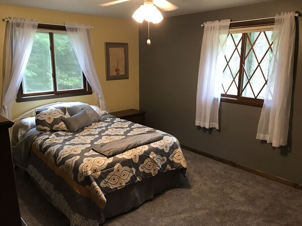 A bedroom with a bed, two windows with curtains, a ceiling fan, and a framed picture on the wall.