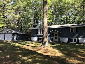 A two-story house with a garage and a front porch, surrounded by trees.