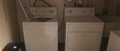 A laundry room with two stacked washers and dryers, a black trash bin, and a white fan.