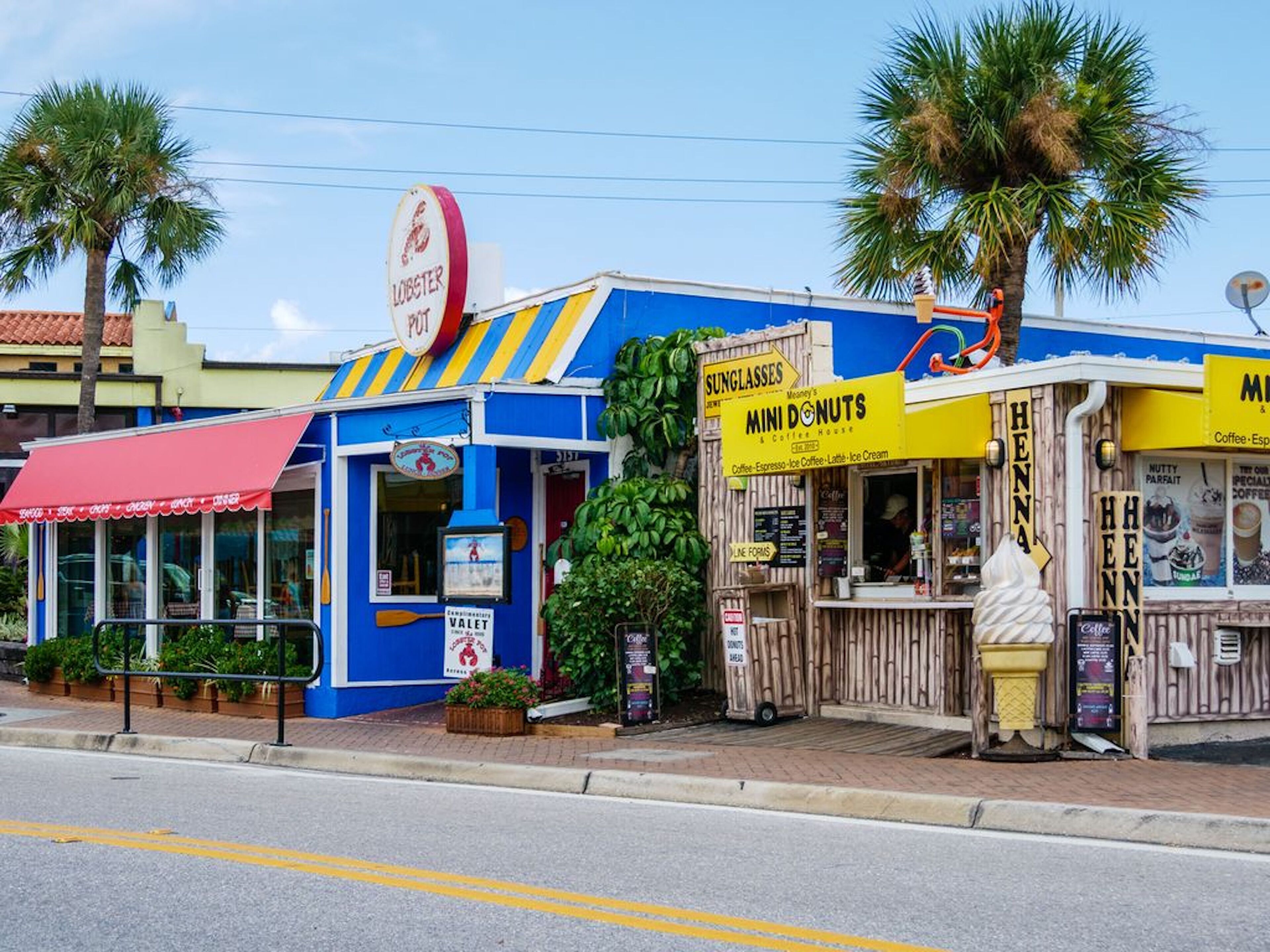 A colorful storefront with a blue awning, a sign for 'Mini Donuts & Coffee House', and a 'Lobster Pot' sign above.