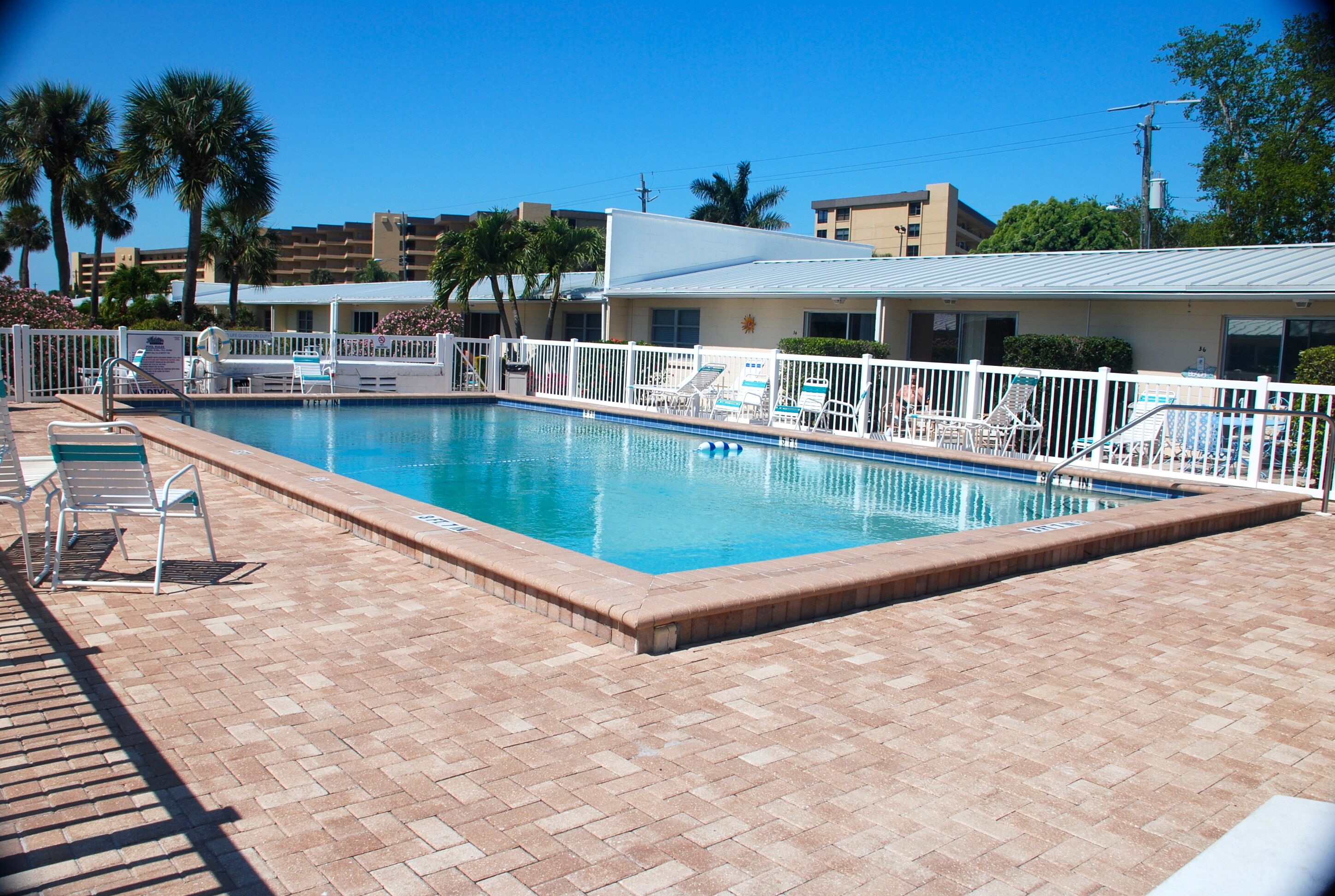 Una piscina con sillas de descanso y un área de terraza cercada.