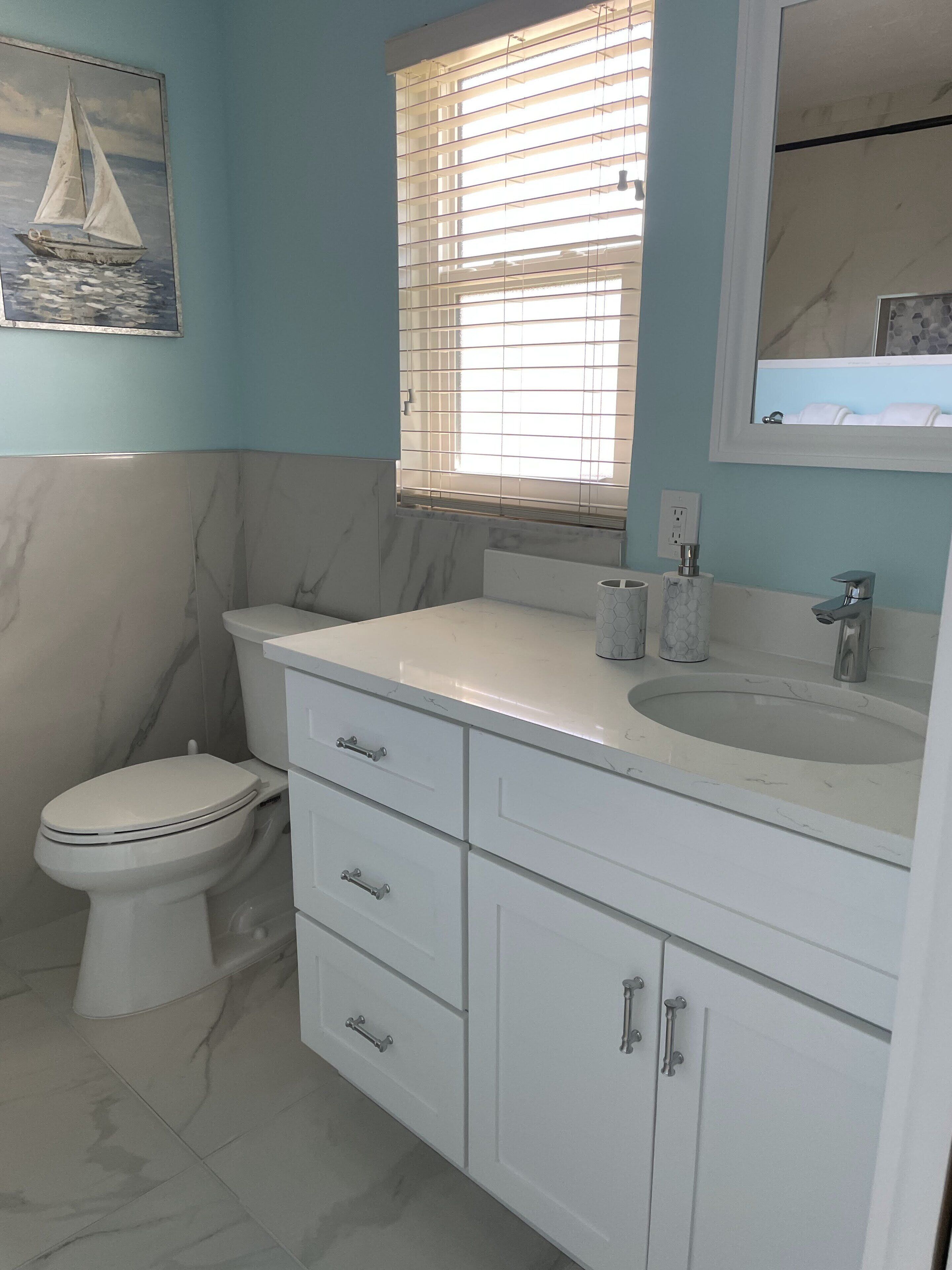 A bathroom with a toilet, a sink with a mirror, and a window with blinds.