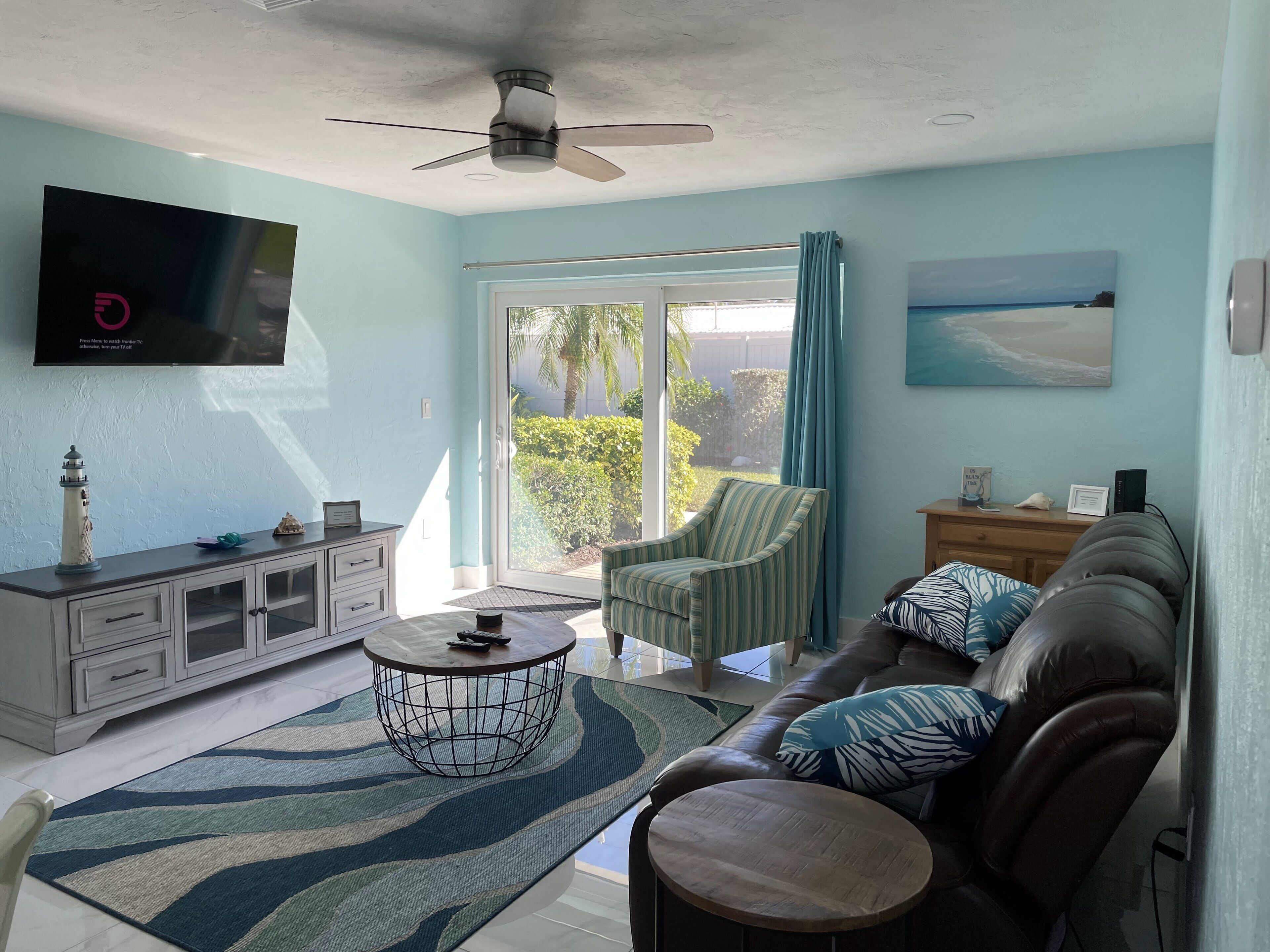 Una sala de estar con televisor, ventilador de techo, sofá, mesa de centro y vistas al exterior.