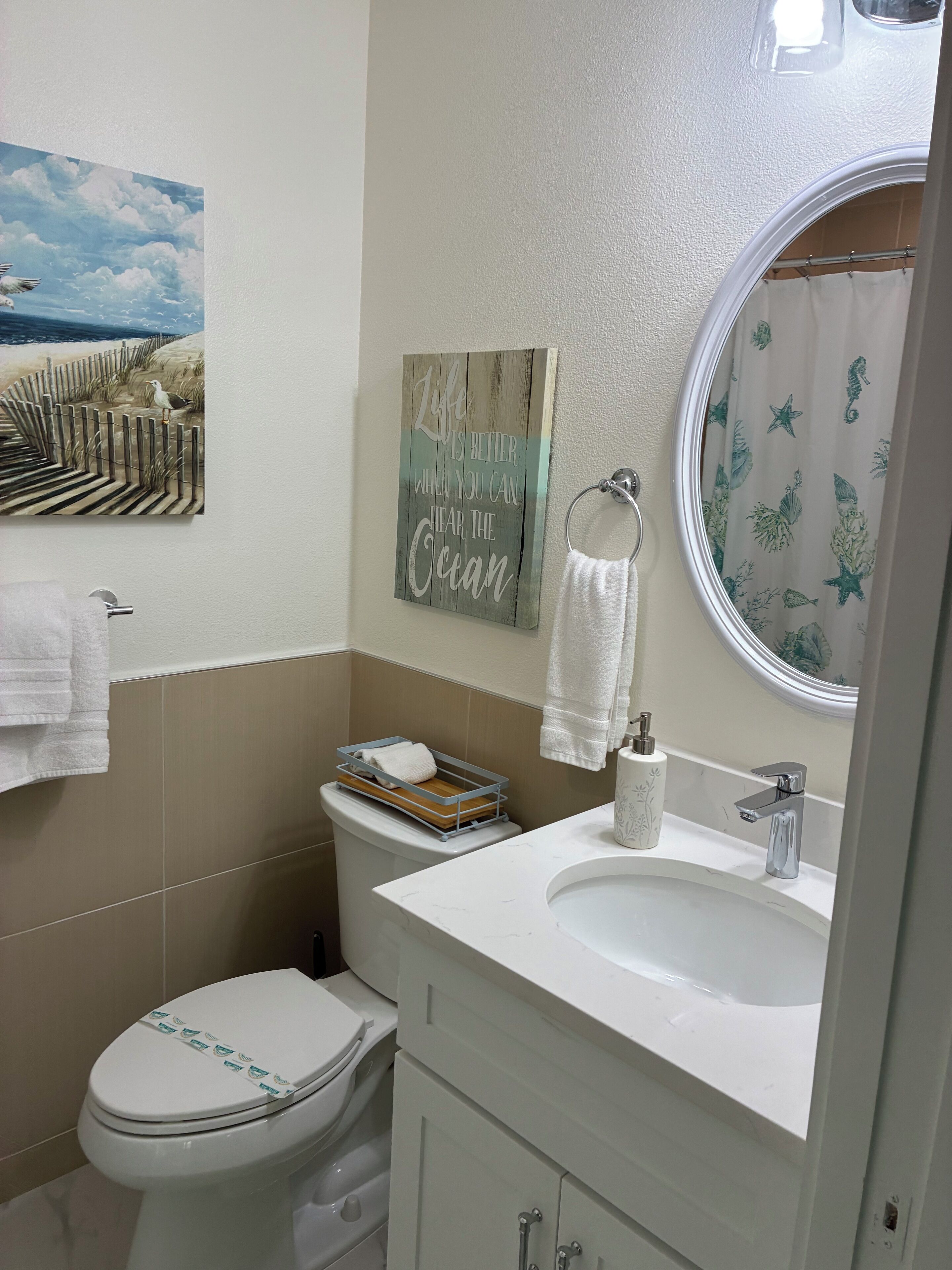 Ein Badezimmer mit Toilette, Waschbecken und Spiegel. Ein Handtuchhalter mit Handtuch und ein dekoratives Schild an der Wand.