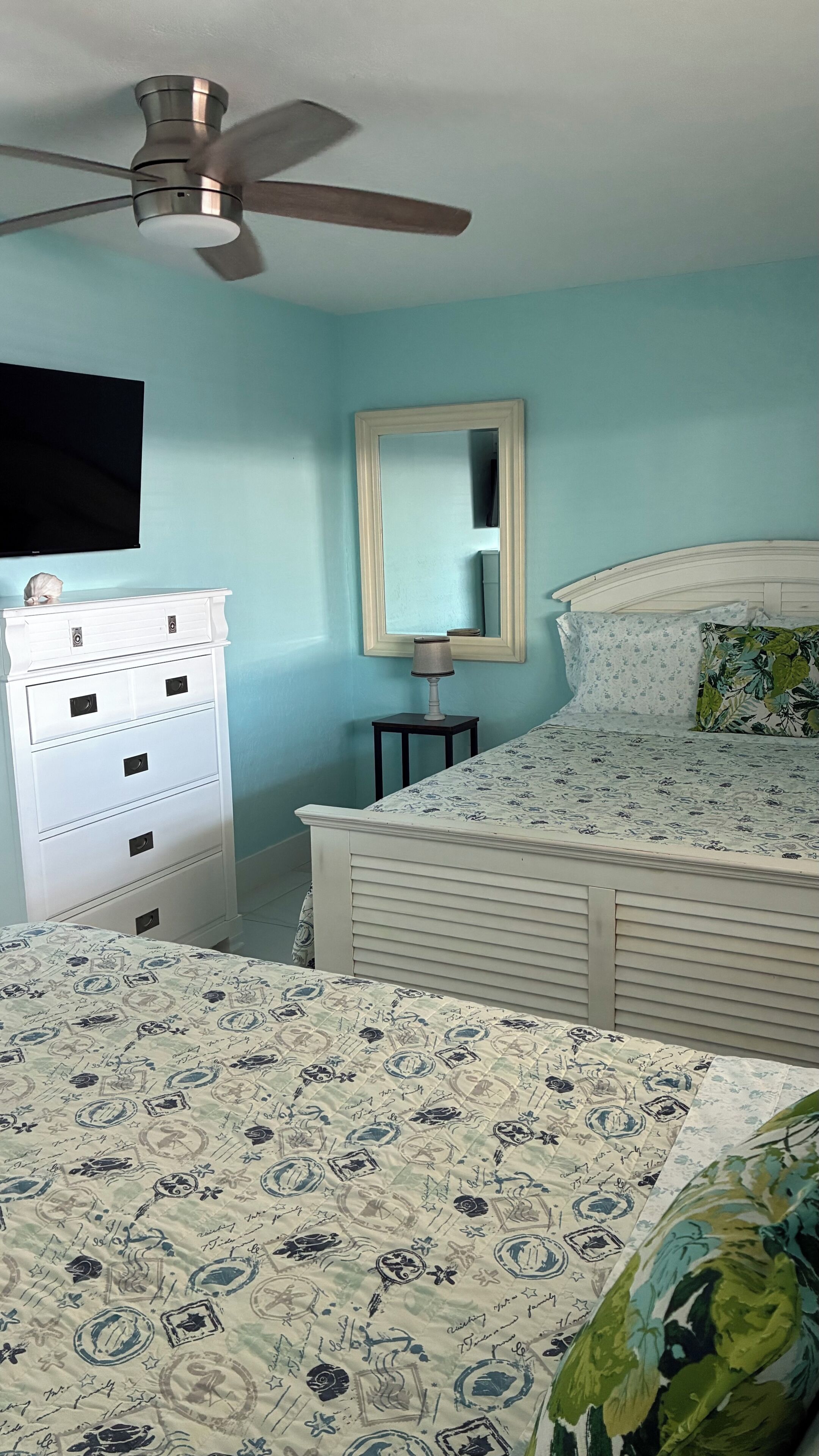 Ein Schlafzimmer mit Bett, Kommode, Deckenventilator und Spiegel.