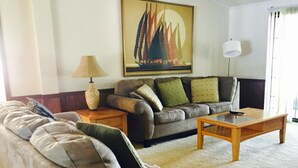 Een woonkamer met een bank, een bijzettafeltje, een lamp en een schilderij aan de muur.