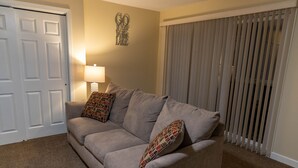 A living room with a beige sofa, patterned pillows, a wall-mounted lamp, and a door. - Luxury Living On The Lake (La Porte)